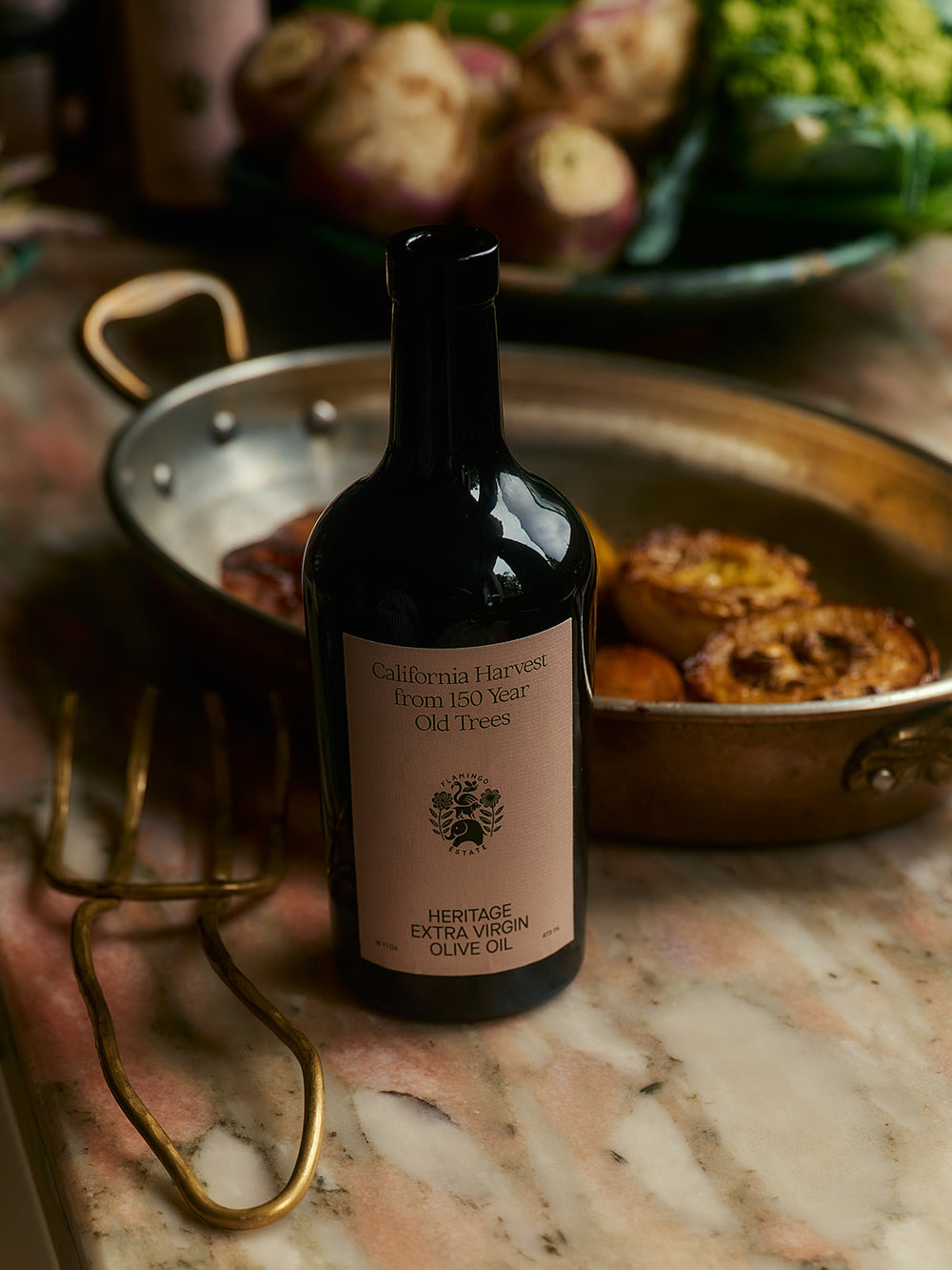 A bottle of wine stands on a table next to pans with cooked meat.
