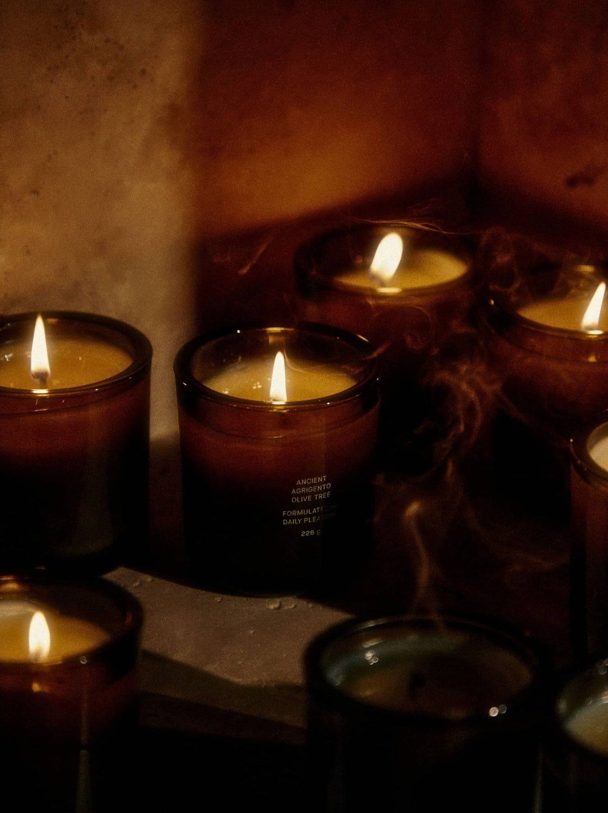 Candles flicker in dim light, releasing wisps of smoke.