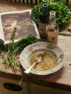 A decorative bowl with a spoon rests on a countertop, holding olive oil.