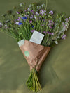 Bouquet Of Green, Blue And Purple Flowers In A Paper Wrap With A Note