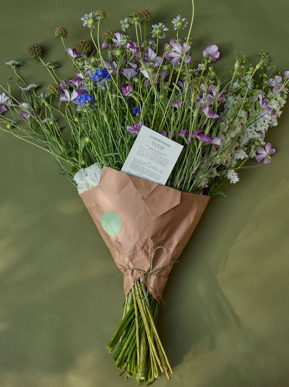 Bouquet Of Green, Blue And Purple Flowers In A Paper Wrap With A Note