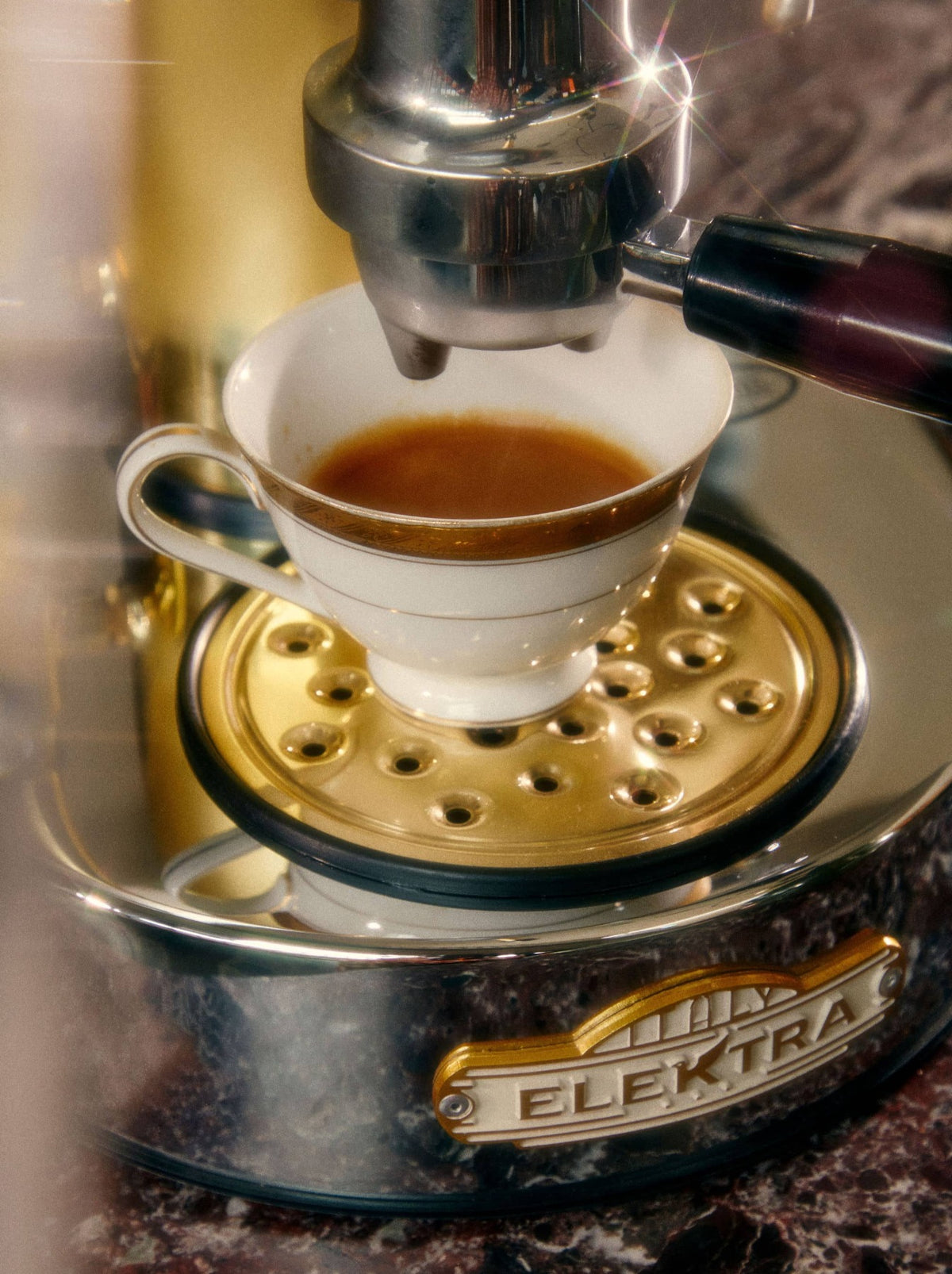 A white cup collects espresso from a metallic coffee machine.