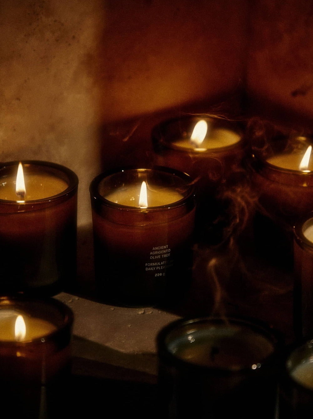 Candles flicker in dim light, releasing wisps of smoke.